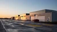 The hangar complex in the glow of the evening sun. The parking area in front of the three closed gates is still empty.