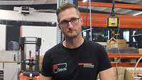Tino Obereigner steht in Arbeitskleidung in einer Fabrikhalle