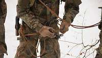 Ein Soldat steht im Schnee und legt seine Kletterausrüstung an.
