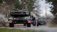 Ein Panzer fährt auf einer Landstraße, zwei Soldaten schauen aus den Luken.