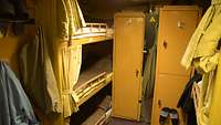 Die enge Schlafkoje der Besatzung an Bord. Rechts steht ein Mehrstockbett mit drei Etagen, vorne stehen zwei schmale Spinde