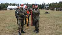 Vier Soldaten halten gemeinsam eine Deutschlandfahne, im Hintergrund sind Soldatinnen und Soldaten angetreten.