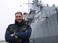 Eine Soldatin steht vor einem grauen Schiff mit verschränkten Armen vor einem grauen Schiff.