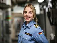 Eine blonde Soldatin steht seitlich zur Kamera und lächelt.