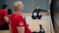 Der Trainer der Sitzvolleyballmannschaft spricht am Volleyballnetz mit den Spielern.