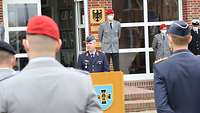 Ein Soldat steht hinter einem Rednerpult und spricht zu den angetretenen Soldaten.