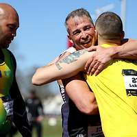 Zwei Männer umarmen sich. Einer steht daneben