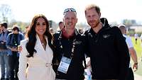 Prinz Harry und seine Frau Meghan posieren zusammen mit einem Sportler in ihrer Mitte