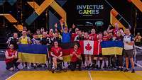 Beide Mannschaften im Sitzvolleyball posieren für ein Gruppenbild mit einer kanadischen, ukrainischen und deutschen Flagge.