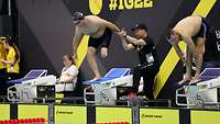 Ein Mann hilft einem einbeinigen Schwimmer auf den Startblock.