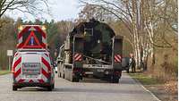 Ein Begleitfahrzeug mit der Aufschrift „Schwertransport“ fährt neben einem Schwerlasttransport mit Kettenfahrzeugen.