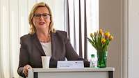 Eine blonde Frau steht an einem Rednerpult und spricht