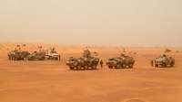 Mehrere gepanzerte Fahrzeuge stehen im Sand in einer Wüstenlandschaft
