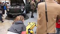 Ein Geländewagen mit offener Motorhaube und ein gelber Roboter werden von Leuten begutachtet.