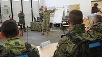 In einer Ausbildungshalle steht ein ungarischer Soldat steht vor einem Flipchart. 
