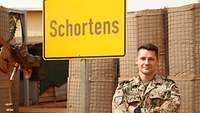 Ein Soldat steht vor einem Ortsschild mit der Aufschrift „Schortens“ 