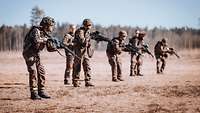 Fünf Soldaten stehen mit ihrem Gewehr in einer Reihe. Hinter ihnen zwei weitere Soldaten