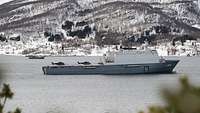 Ein graues Schiff liegt in einem Fjord.