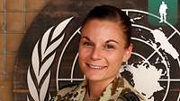 Eine Soldatin im Portrait vor einer Holztafel mit dem UN-Wappen