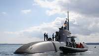Ein U-Boot liegt aufgetaucht in See; davor ein Festrumfpschlauchboot auf dem Wasser.