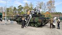 Soldaten und Zivilisten steigen über eine angelehnte Alutreppe auf einen Kampfpanzer.