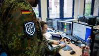 Ein Soldat schreibt einen Bericht auf dem Computer. Ein Offizier blickt ihm dabei über die Schulter.