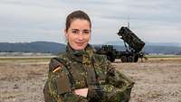 Eine Soldatin im Portrait. Im Hintergrund steht das Flugabwehrraketensystem Patriot.