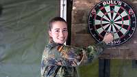 Eine Soldatin steht vor einer Dartscheibe und zieht einen Pfeil heraus