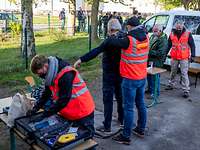 Durchsuchung am Sammelpunkt Männer mit leuchtend roten Warnwesten durchsuchen Personen und Koffer.
