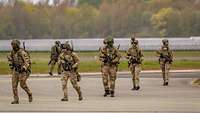 Mehrere Soldaten der niederländischen Armee laufen mit Waffe auf einem Flugfeld.