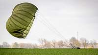Fallschirmladung beim Schnellen Adler Ein Soldat landet mit seinem grünen Fallschirm auf einem Feld.