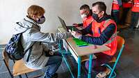 Krisenunterstützungsteam bei der Registrierung Zwei Personen in roten Warnwesten sitzen einer Zivilperson einem Tisch gegenüber.