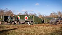 Auf einer freien Fläche stehen grüne Zelte, Militärfahrzeuge und Container mit dem Rotkreuz-Symbol.