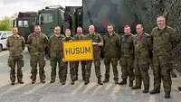 Generalleutnant Gehartz beim Erinnerungsfoto mit der Truppe. Sie halten ein Schild mit dem Schriftzug „Husum“.