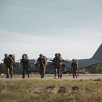 Auf einem Flugplatz steht ein großes, graues Flugzeug, davor laufen mehrere Soldaten.