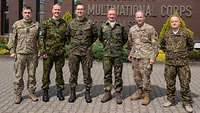 Soldaten in Uniformen verschiedener Länder stehen nebeneinander vor einem Backsteingebäude.