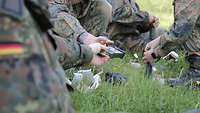 Soldaten knieen auf einer Wiese und munitionieren Gewehrmagazine mit Patronen auf.