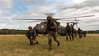 Bewaffnete Soldaten verlassen einen Transporthubschrauber, der in freiem Gelände steht.