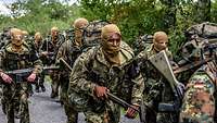 Angehende bewaffnete Kommandosoldaten marschieren mit verhülltem Gesicht und schwer bepackt.