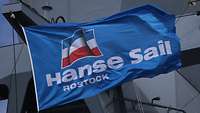 Eine blaue Flagge mit der Aufschrift „Hanse Sail Rostock“ weht im Wind.