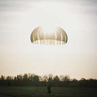 Ein Soldat landet im Morgenlicht mit seinem Fallschirm auf einem Feld.