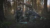 Einweisung durch das Combat Control Team (CCT) Zwei Soldaten knien im Wald. Einer zeigt mit der Hand in eine Richtung.