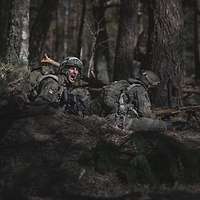 Soldaten liegen in Stellung im dunklen Wald. Einer wendet seinen Blick und schreit.