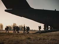 Die Verstärkung landet Mehrere Soldaten steigen im Morgengrauen aus der Heckrampe eines großen Flugzeuges.