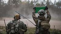 Fallschirmjäger treffen auf die eFP-Battlegroup Zwei Soldaten stehen an einer Waldkante und halten ein grünes Tuch hoch, vor ihnen Panzer.