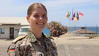 Eine Soldatin steht im Camp Martin vor einem Flaggenmast und blickt in die Kamera