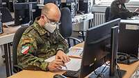 Ein Soldat arbeitet am PC und wertet Unterlagen aus.