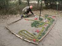 Ein Soldat kniet auf dem Boden und platziert Markierungspunkte in einer im Sand angelegten taktischen Lagekarte