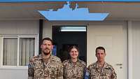 Eine Soldatin und zwei Soldaten vor der offenen Eingangstür des NOC im Portrait