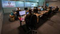 Sieben Soldaten sitzen in zwei Reihen und arbeiten an Computern. Im Hintergrund Screenshots über Beamer an der Wand sichtbar.